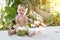 Teething and salivation infant baby at tropical vacation. Eats and drinks green young coconut. Sits on a ground and gnaw a spoon.