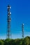 Telecommunication masts TV antennas wireless technology against blue cloudless sky over green hedges