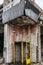 Telephone booth in a building with broken windows, shabby entrance in marble, with overgrown trees and grass in abandoned town of