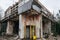 Telephone booth in a building with broken windows, shabby entrance in marble, with overgrown trees and grass in abandoned town of