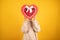 Ten years old boy holding a heart-shaped gift box in his hand, no face.Teen boy in biege hoodie on yellow background.