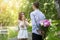 Tender boyfriend hiding bouquet of beautiful peonies for his girl behind his back in park