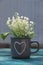 Tender, fragrant lilies in brown cup with a heart on a green wooden table