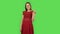 Tender girl in red dress is showing two fingers victory gesture. Green screen
