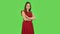 Tender girl in red dress is smiling while looking at camera and crossing her arms on chest. Green screen