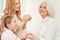 Tender grandchild and mom applying cream on face of grandmother