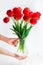 Tender hands hold tulips bouquet in vase on wood table