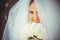 Tender happy bride in veil, happy woman in wedding dress with bouquet in hands, white veil covers face, gentle and warm