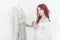 Tender portrait of a young dreamy redhead woman in nightdress. She is standing in dress room and planning to wear beautiful vintag