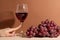 Tender woman finger touch the wineglass with red wine with branch of grapes background. Beige surface