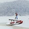 Tenderly hugging couple in the front of the snowy boat near the forest during the snowfall.