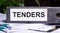 TENDERS is written on a gray file folder next to documents. Business concept