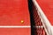 A tennis ball on the textured floor of a red court near the net after losing a match point