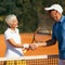 Tennis Instructor with Senior Woman in her 60s Handshaking after Having a Tennis Lesson on Clay Court