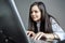 Tense young woman working on laptop in office. Funny image of young Caucasian Asian businesswoman.