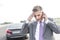 Tensed businessman talking on mobile phone against breakdown car
