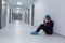 Tensed female surgeon with hands on forehead sitting on floor in the corridor at hospital