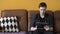 Tensed man in black shirt using his tablet while sitting on brown leather couch at home. Stock footage. Stressed hipster