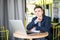 Tensed young man working on laptop at cafe table and thinking