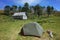 Tent on green grass by old wooden house and small forest on hill, Summer vacation, Camping at Refugio El Caulle