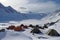 tents and shelters in a snowy landscape, with mountains in the background