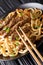 Teriyaki beef with udon noodles, carrots and green onions close-up on a plate on the table. vertical