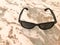 Ternary sun-baked plastic glasses with black glass and bows lie on a brown sand-colored light stone with multi-colored mottled sti