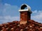 Terracotta clay roof detail with brick chimney under blue sky