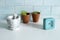 Terracotta pots with a small light blue table clock and a grey marble mortar on white table and ceramic blue wall.