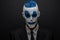 Terrible clown and Halloween theme: Crazy blue clown in black suit isolated on a dark background in the studio