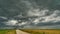 A terrible rain cloud hangs over an agricultural field and a dirt road. Hurricane and thunder over a green meadow. Climate change