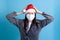 terrified Asian young woman wearing Santa Claus hat and medical protective mask on face, holding head with her hands