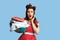 Terrified millennial pinup woman holding clothes for washing or ironing on blue studio background