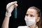 A test tube with a green luminous substance liquid in the hand of a young woman in a mask, a scientific specialist or