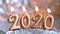 Text 2020 golden candles burning. Blurred glitter silver background. Merry christmas and Happy New Year. Selective