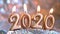 Text 2020 golden candles burning. Blurred silver background. Merry christmas and Happy New Year. Selective focus