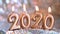 Text 2020 golden candles burning. Blurred silver background. Merry christmas and Happy New Year. Selective focus