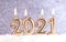 Text 2021, burning melting candles in the snow, on a blurred silver background with bokeh. Christmas and New Years concept.