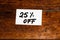 Text 25% off on white label. Label on wooden table, close up