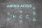 Text AMINO ACIDS and chemical formula on light grey stone surface