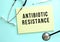 The text ANTIBIOTIC RESISTANCE is written in a yellow pad that lies next to the stethoscope on a blue background.