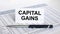 Text Capital Gains on white card with blue metal pen on financial table