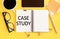 Text is a case study written  in a notebook and office supplies on a yellow table