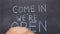 Text come in we`re open, written with chalk on old blackboard.