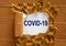 The text `covid-19` appearing behind torn brown paper. Yellow pills. COVID-19 Pandemic Coronavirus and business concept