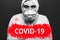Text covid-19 on red warning sign on portret of man in biohazard chemical protective suit and face mask. Coronavirus pandemic