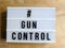 Text in english on lightbox sign spelling   Gun Control. Against wood background