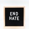 Text in english spelling `End Hate` on black felt board in a wooden frame. Letter Board on white background. A sign with a messa