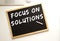 Text FOCUS ON SOLUTIONS written in chalk on a slate board. Office desk.