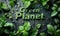 Text Green Planet embossed on a dark, wet surface surrounded by fresh, dewy green leaves symbolizing environmental